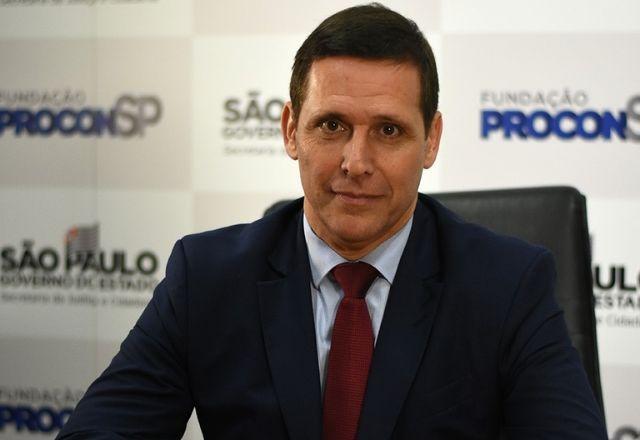 fernando capez, de terno, em frente a um banner do Procon
