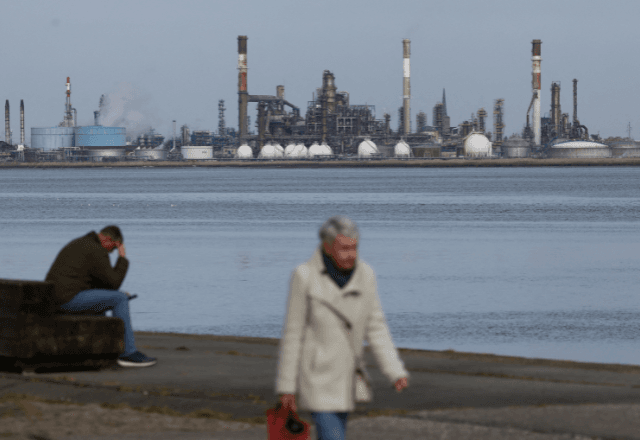 Uma mulher caminha em frente à refinaria da gigante petrolífera francesa TotalEnergies em Donges, perto de Saint-Nazaire, na França | Foto: reprodução/Reuters